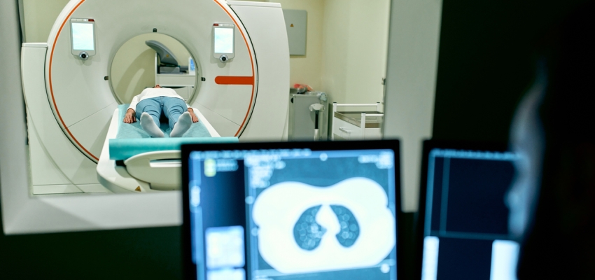 A patient undergoes an MRI or CT scan under the supervision of a radiologist in the control room.