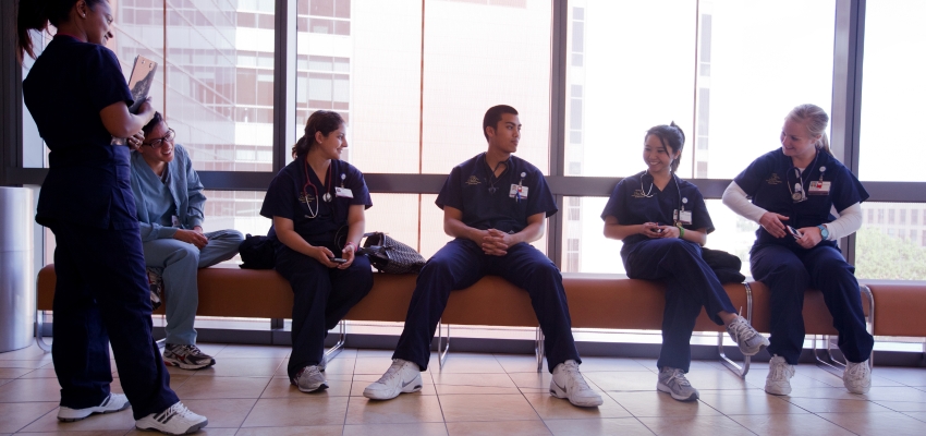 A group of UCI Nursing students wearing their scrubs and sitting on a bench in front of a window