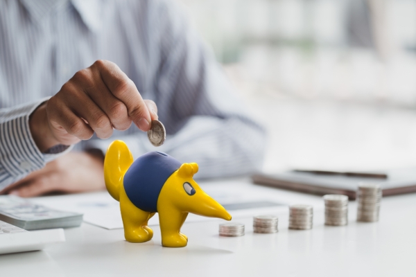 A person putting a coin in to a Anteater piggy bank with a 5 stacks of coins next to it.