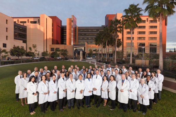 A large group of UCI doctors standing in white coats in front of the UCI Medical Center