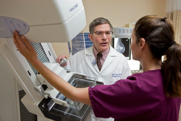 Doctor and trainee part of the UC Irvine Department of Radiological Sciences Breast Imaging Division stand near 3-D mammography machine