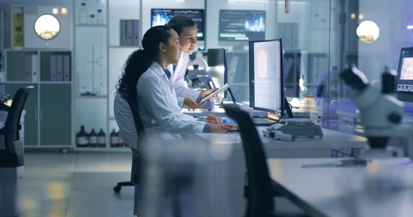 Two people in white lab coats looking at a computer screen in a laboratory.