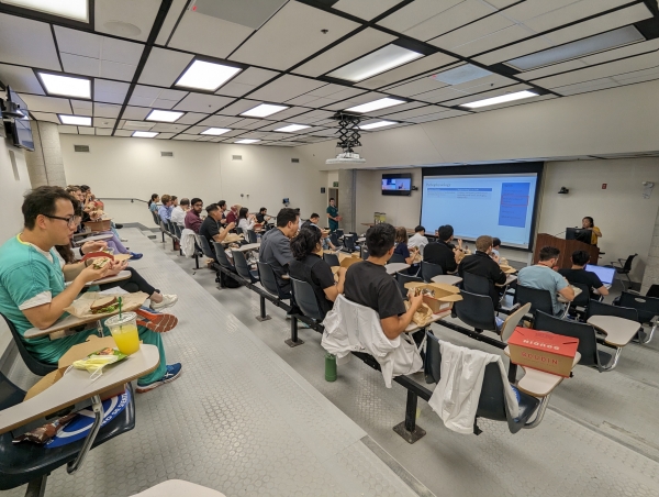 A lecture hall with attendees seated at tiered desks, viewing a presentation titled "Pathophysiology" on a large screen.