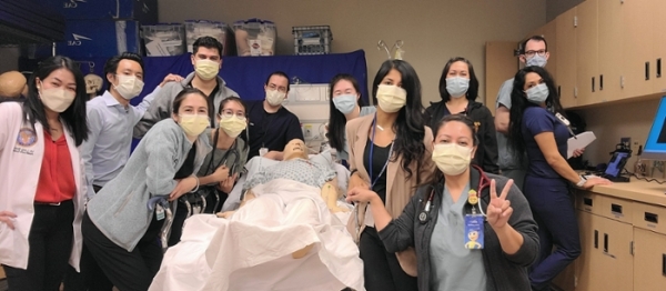 Group of medical residents posing around a teaching dummy on a gurney.