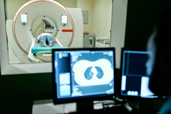 A patient undergoes an MRI or CT scan under the supervision of a radiologist in the control room.