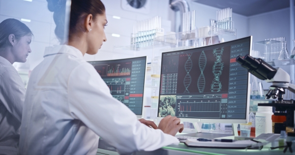 Female research team studying DNA mutations. Computer screens with DNA helix in foreground stock photo