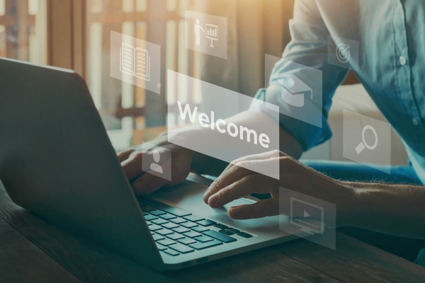 Person typing on a laptop with digital icons and the word "Welcome" floating around.