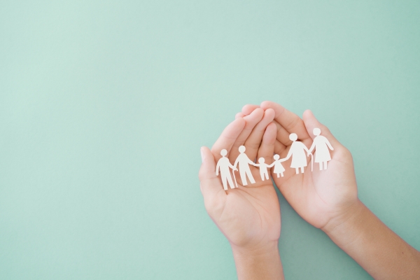 Hands holding multi generation paper cutout family above light green background.