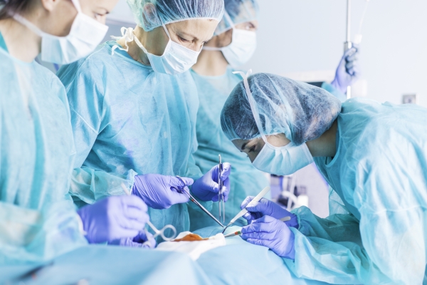 Team of 4 medical professionals in surgical gowns performing surgery in an operating room.