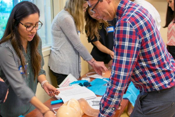 People practicing medical procedures on a mannequin in a classroom setting.