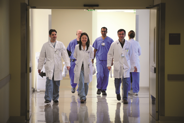 A group of six UCI doctors in white coats walking down a hospital hallway