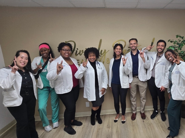 PRIME LEAD-ABC students visited Divinely Restored Health & Wellness for Harvest Elective – A group of eight people in white lab coats posing indoors with hand gestures.