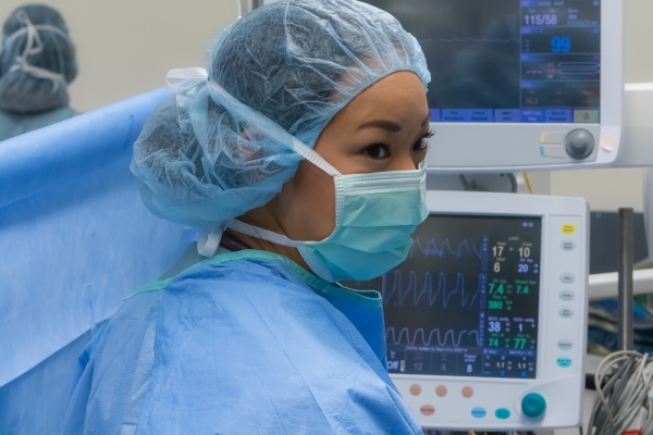Healthcare professional in surgical attire monitoring vital signs on medical screens.
