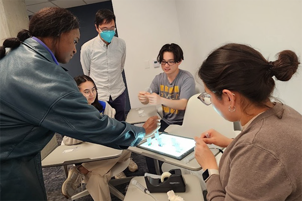 A group of students sit around a four desks working on a technical project as part of the Physician Innovator Training Program