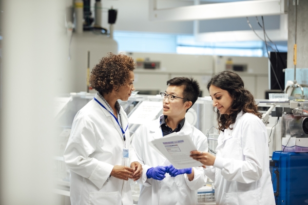 Three people in lab coats in a lab in discussion