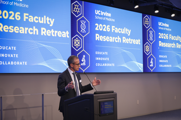 Dean Stamos at a podium in front of a screen displaying "2026 Faculty Research Retreat" and UC Irvine School of Medicine visuals.
