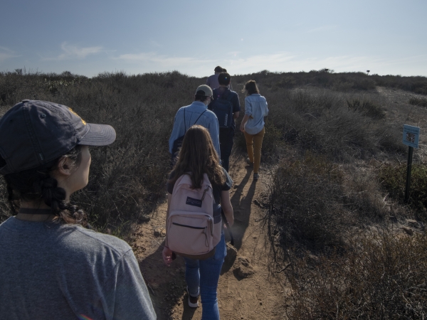 A group hiking on a nature trail in Irvine with the sun shining brightly in the sky