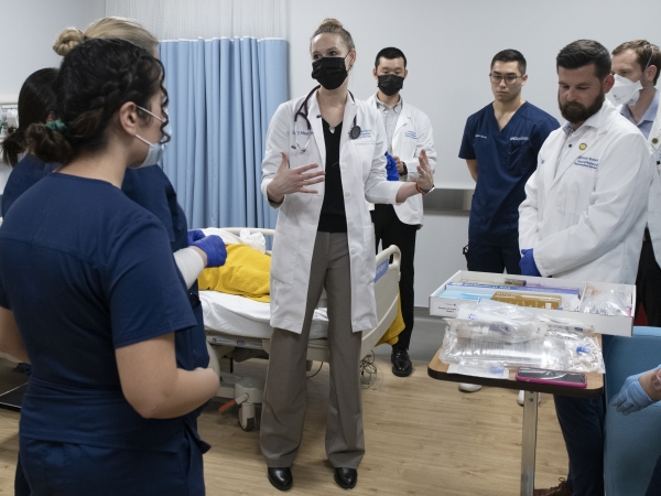 A group of medical students in a practice hospital room getting instructions from a teaching doctor