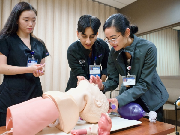 Three individuals practicing on the mouth of a mannequin with lungs opening up airway in a training room