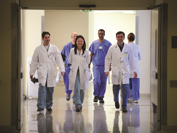 A group of six UCI doctors in white coats walking down a hospital hallway