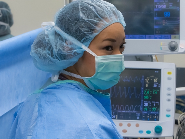 Healthcare professional in surgical attire monitoring vital signs on medical screens.