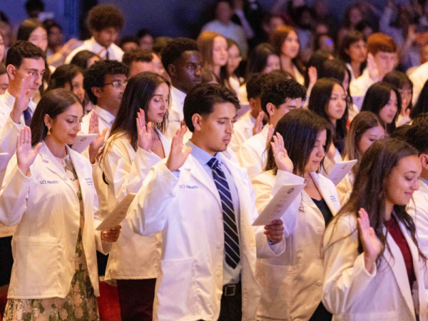 A group of students, standing in white coats with their right hands raised while reciting an oath.