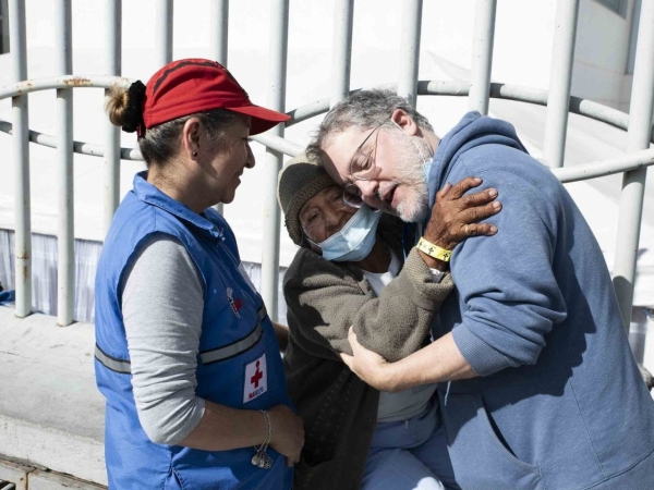 Doctor embraces elderly woman alongside a medical worker.