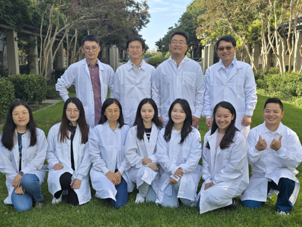 11 people, four standing, 7 kneeling, all wearing white lab coats