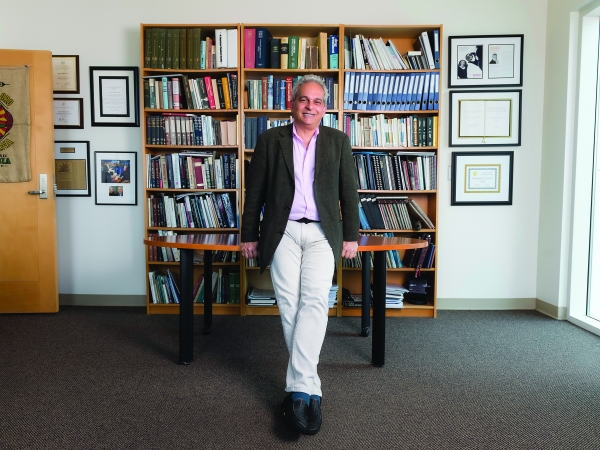 Daniele Piomelli standing in front of a table and bookshelves in his office