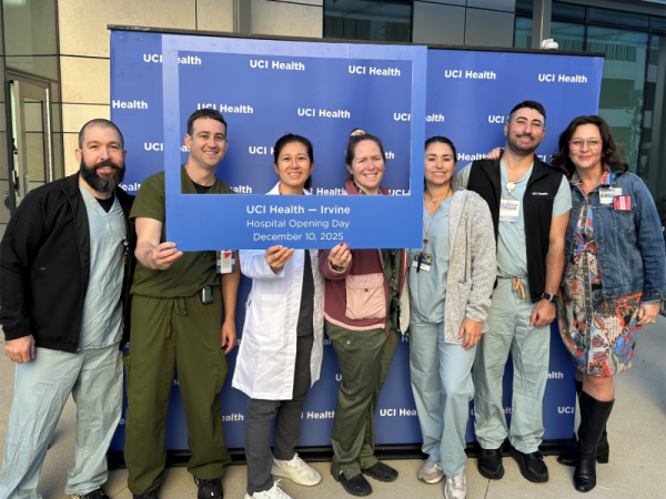 Seven people (all but one wearing scrubs) in front of a UCI Health step-and-repeat backdrop, and three (including Nahmias) are holding a sign that says UCI Health - Irvine, Hospital Opening Day, December 10, 2025.