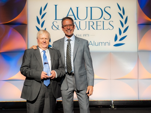 Harry Herr holds an award next to Dean Stamos while on stage at 2024 Lauds & Laurels alumni award ceremony.