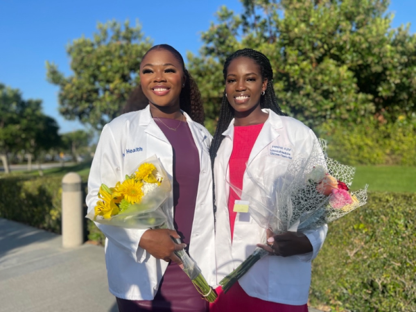 Mary Aina and Femitan Ajayi stand together outside, holding flowers and wearing their white coats