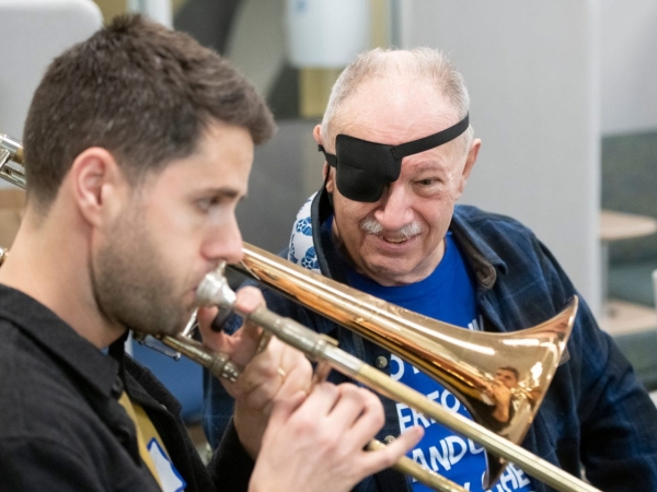 Trombonist playing next to a stroke patient wearing an eye patch. 