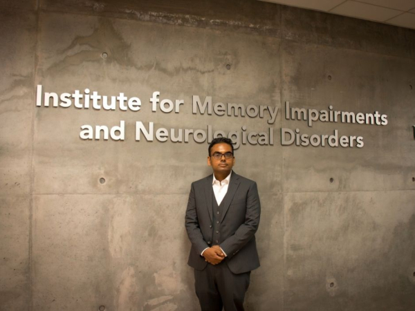 Vivek Swarup, Ph.D., standing against the Institute for Memory Impairments and Neurological Disorders wall
