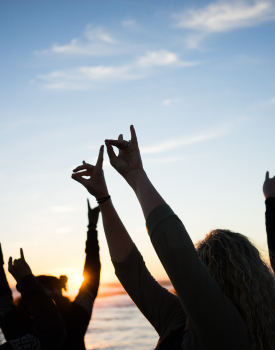 Students on the beach watching the sunset making ZOT hand silhouettes in the sky.
