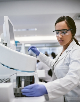 Person using lab equipment wearing a white lab coat and purple gloves.