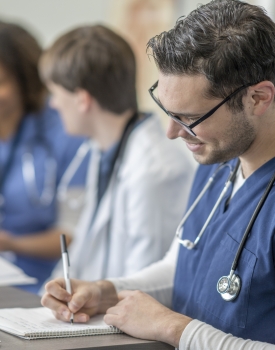 Group of healthcare students wearing scrubs attending class together, seated in a classroom doing course work.