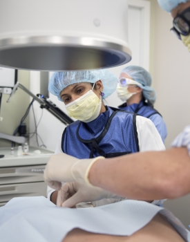 A trainee watches a faculty anesthesiologist provide care to a patient in an operating room 