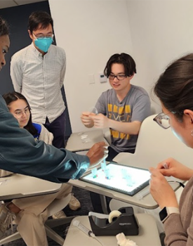 A group of students sit around a four desks working on a technical project as part of the Physician Innovator Training Program