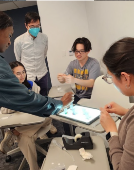 A group of students sit around a four desks working on a technical project as part of the Physician Innovator Training Program