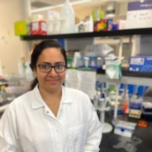 Asha Densi, PhD, postdoc at UCI, wearing a whitecoat in a campus lab