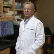 Lbachir BenMohamed stands in a lab, wearing a white lab coat.