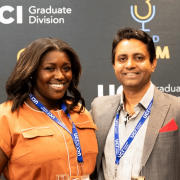 Two people posing for a photo in front of a UCI Grad Division banner