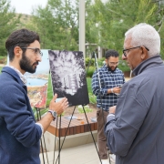 Clifford Danza and Chalat Rajaram, MD, converse about Danza's photo in the background of this outdoor symposium.