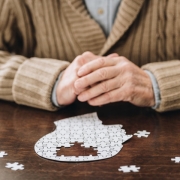Elderly person with their hands folded on table with puzzle in the shape of a person's head