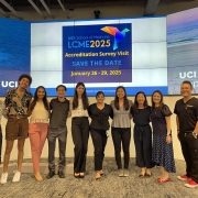 A bunch of students standing in front of a large video screen that is labelled UCI LCME2025 - Accreditation Survey Visit, save the Date, January 26 - 29, 2025