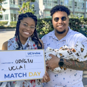 Avery holds a sign that says: “UC Irvine School of Medicine Match Day. I matched in OB/GYN at UCLA!” Standing next to her is her husband, who is holding their baby wrapped in a blanket.
