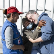 Doctor embraces elderly woman alongside a medical worker.
