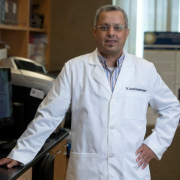 Lbachir BenMohamed in a white coat standing in lab. 
