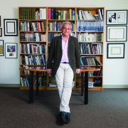 Daniele Piomelli standing in front of a table and bookshelves in his office